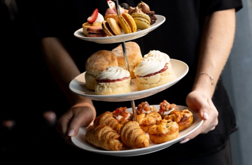 Person holding tiered food holder with savoury and sweet selection of food on offer