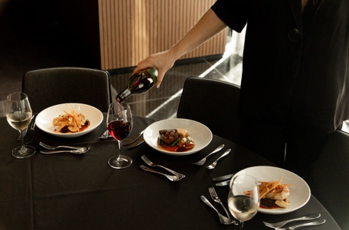 Person pouring wine into wine glass at table with multiple main meals served